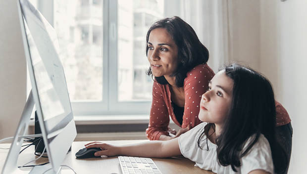 A mother and daughter working together at a computer, natural window light filling the room